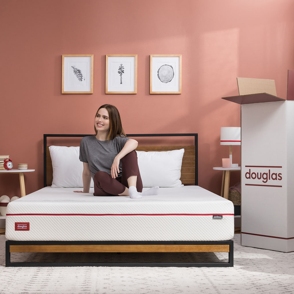 Woman enjoying sitting on her recently unboxed Douglas mattress in a vibrant bedroom