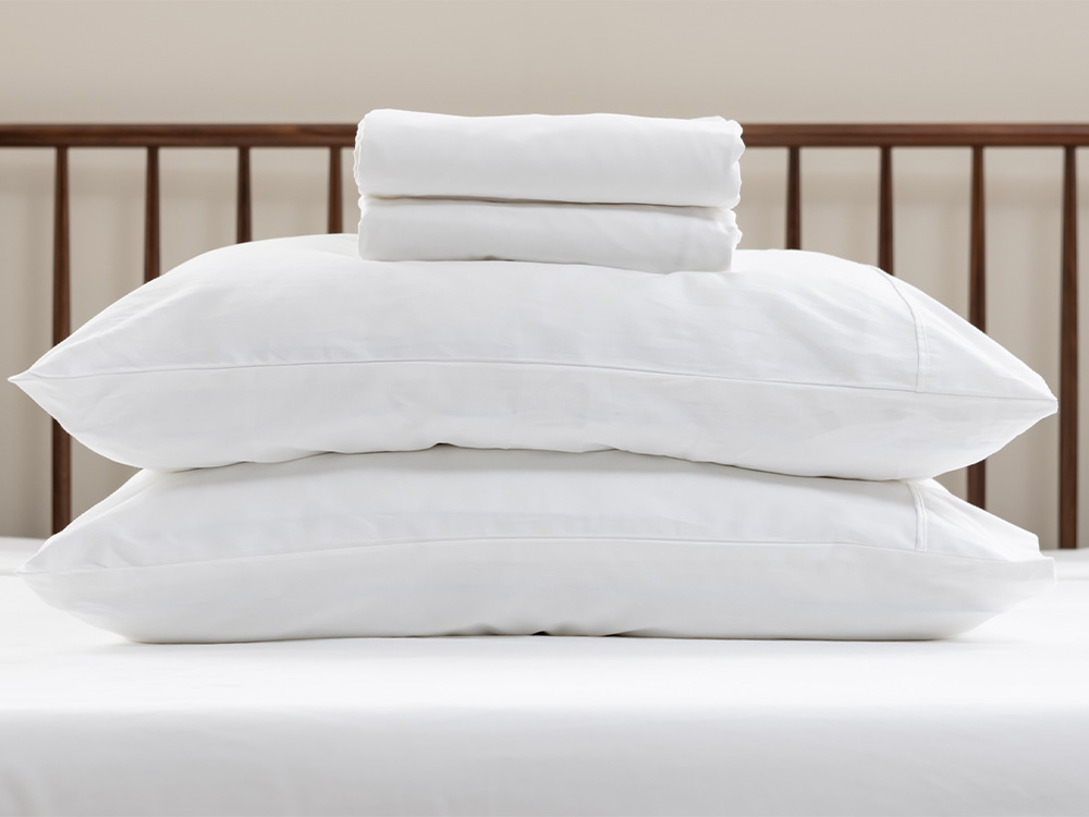 Sateen cotton sheets fitted to two pillows, stacked on a bed