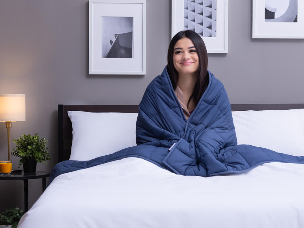 Woman seated in bed with Classic Weighted Blanket hugged around her shoulders