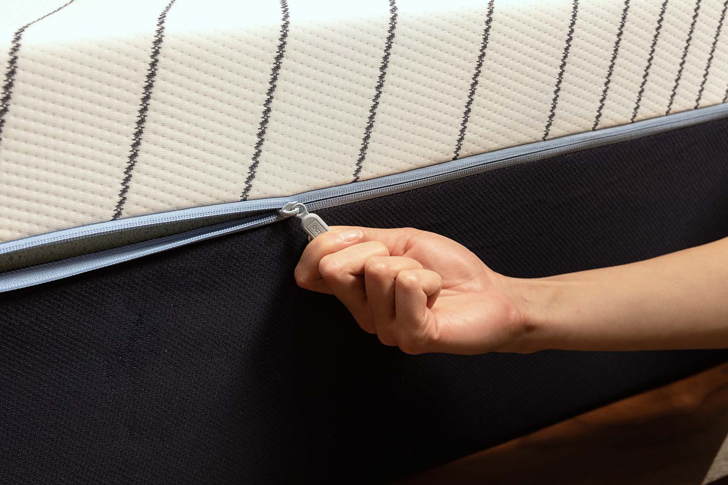 Close-up view of the Octave mattress cover, with a hand pulling the zipper.
