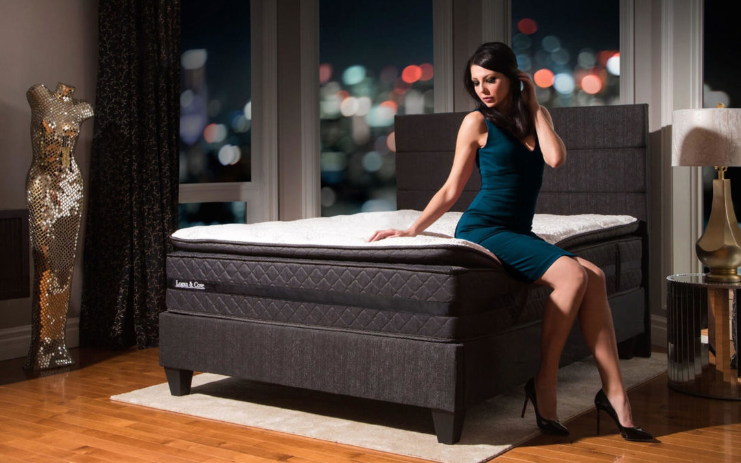 Woman sitting on the edge of the Logan & Cove luxury hybrid pillow-top mattress with a colourful city night sky in the background