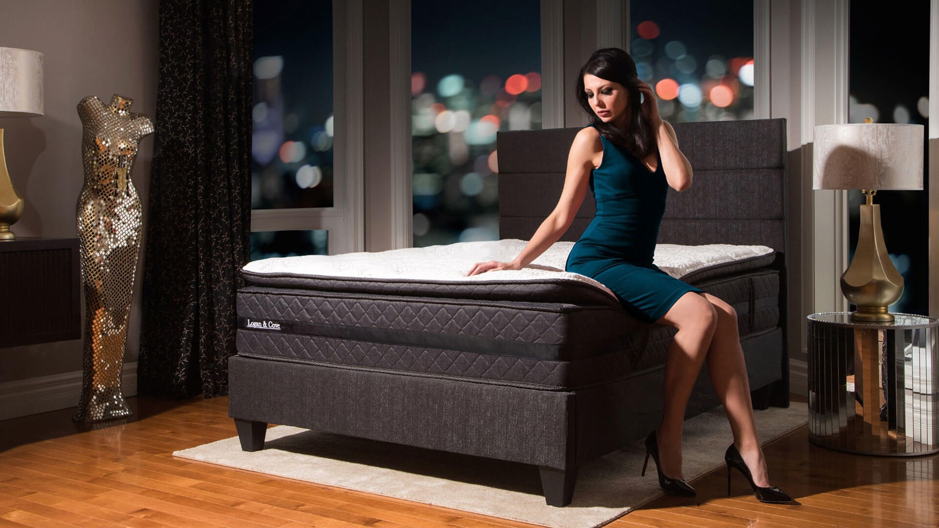 Woman sitting on the edge of the Logan & Cove luxury hybrid pillow-top mattress with a colourful city night sky in the background