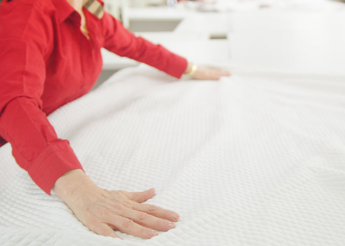 Image of a mattress factory worker in a bright red work shirt smoothing out the white fabric for the Douglas mattress cover.