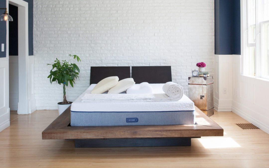 A Novosbed by Goodmorning.com sits on a raised wood platform in a bright, white room.