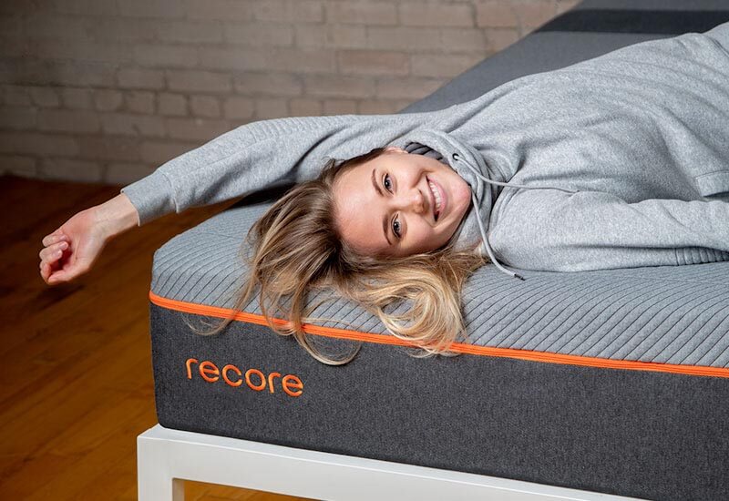 Smiling young woman in athletic clothes lying atop the Recore performance latex mattress