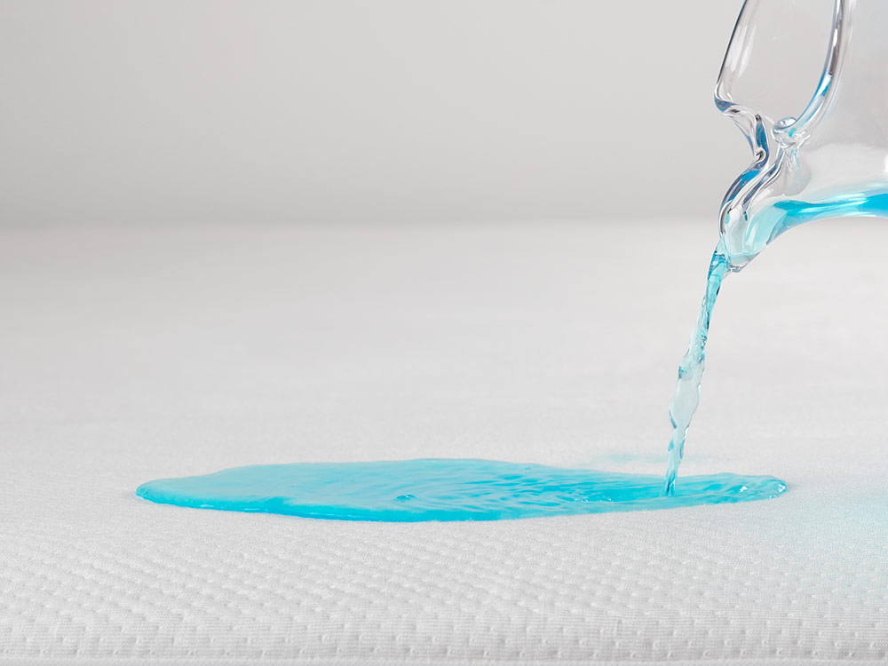 Blue liquid being poured on mattress protector.